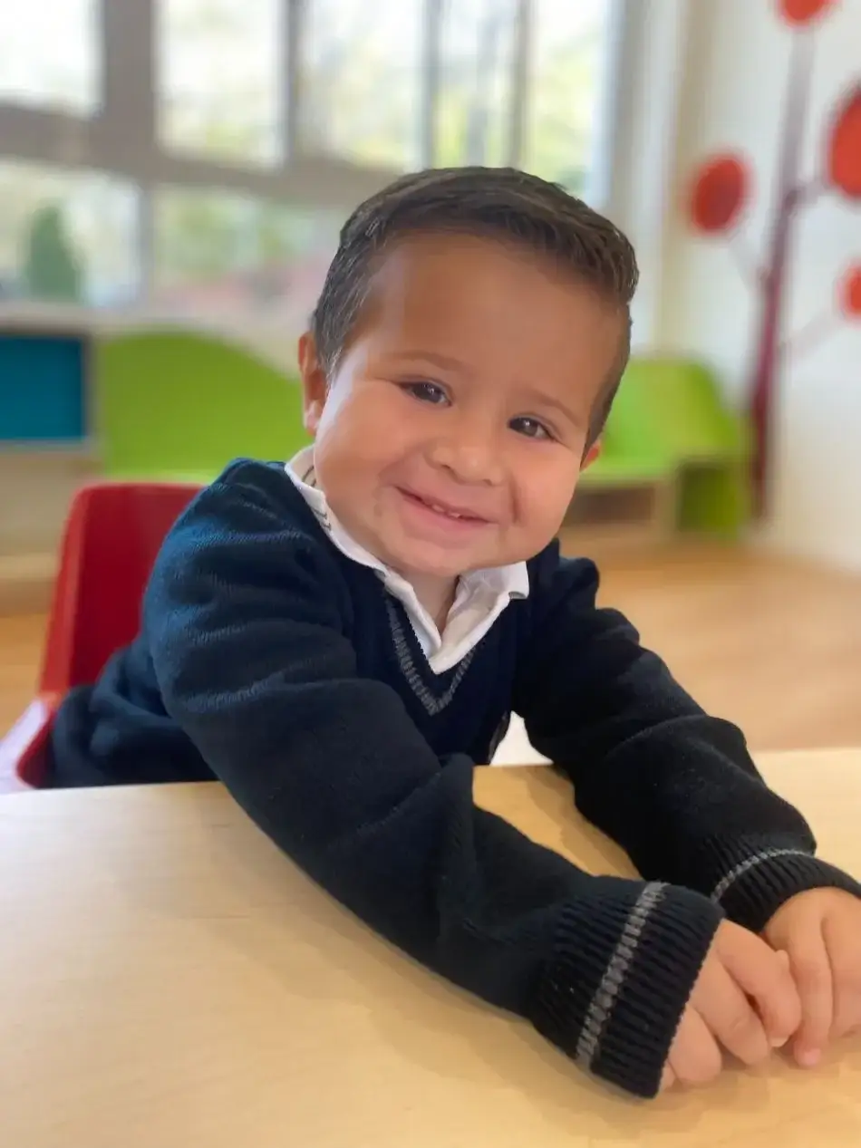 Niño pequeño sonriendo en el aula durante actividades escolares en ambiente educativo